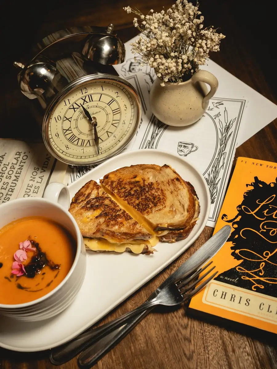 Grilled cheese con sopa de tomate junto a un reloj antiguo