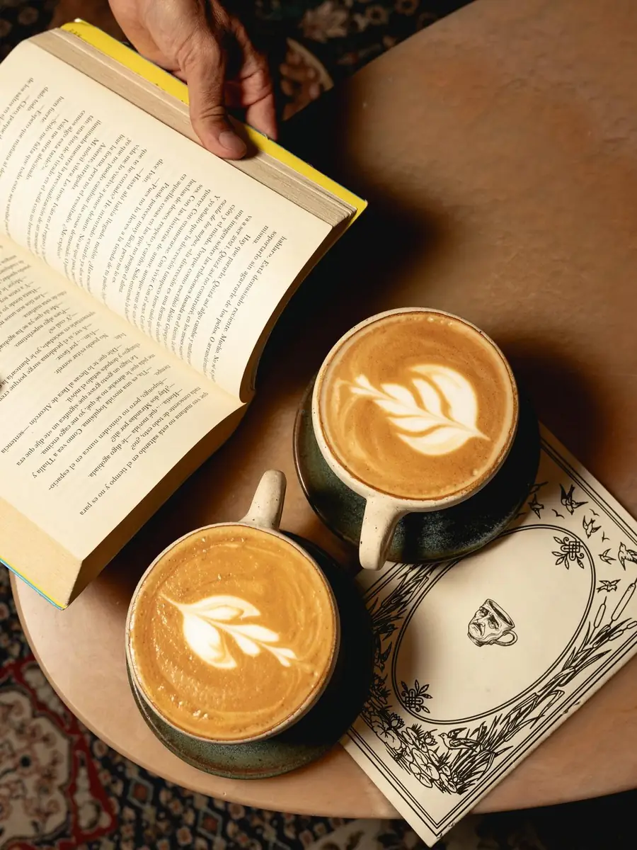 Dos capuchinos con arte latte junto a un libro abierto