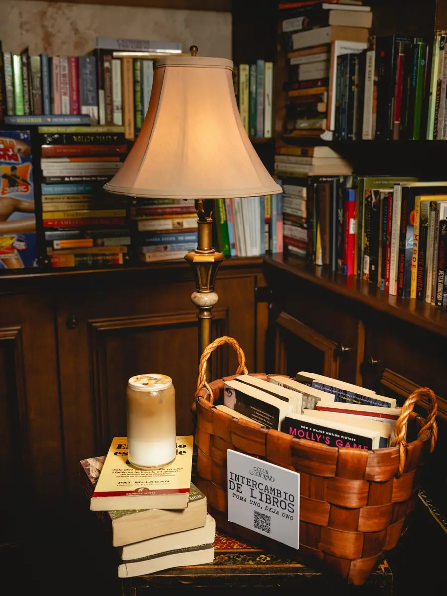 Lámpara encendida entre estanterías y una canasta con libros